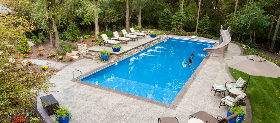 A picture of in ground pool with chairs and a slide around it.