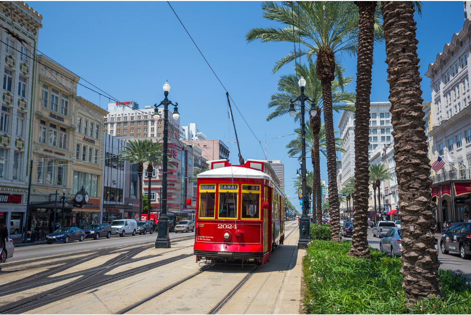 A picture of a red street car with buildings on each side in New Orleans, LA.