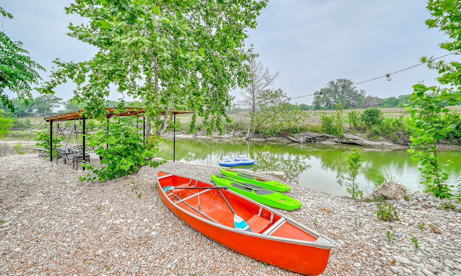 A red canoe and two green kayaks are sitting on the shore of a lake.