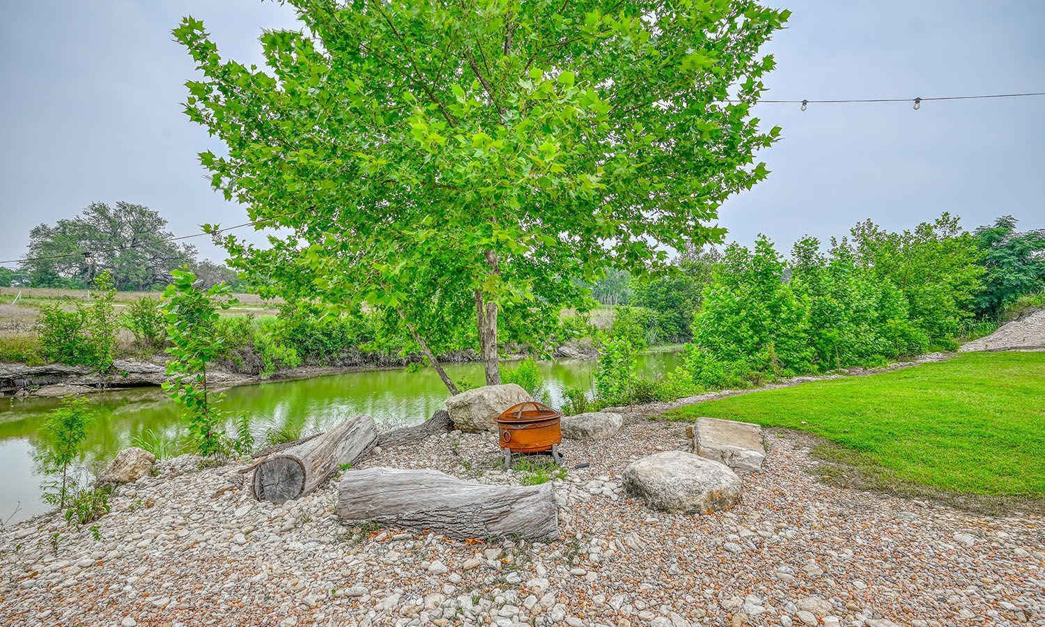 A fire pit is sitting in the middle of a rocky area next to a tree.