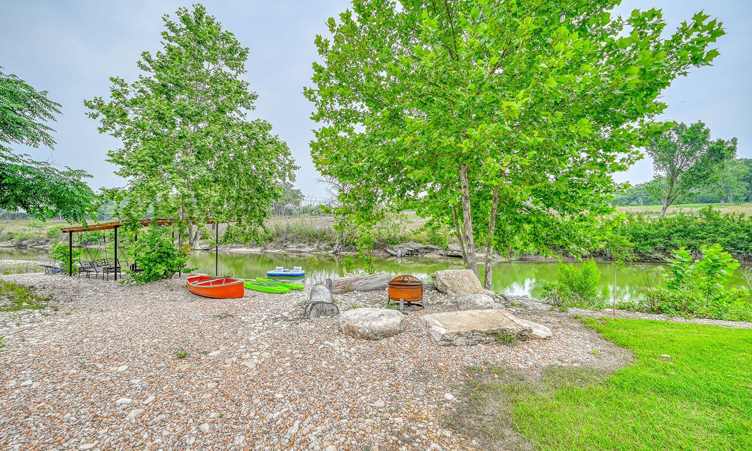 A fire pit in the middle of a grassy field next to a body of water.