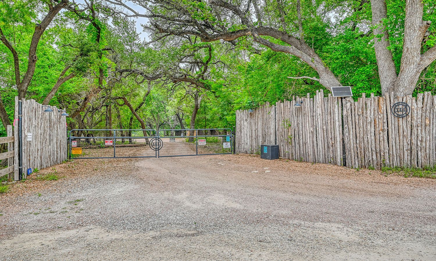 A dirt road leading to a wooden fence surrounded by trees.