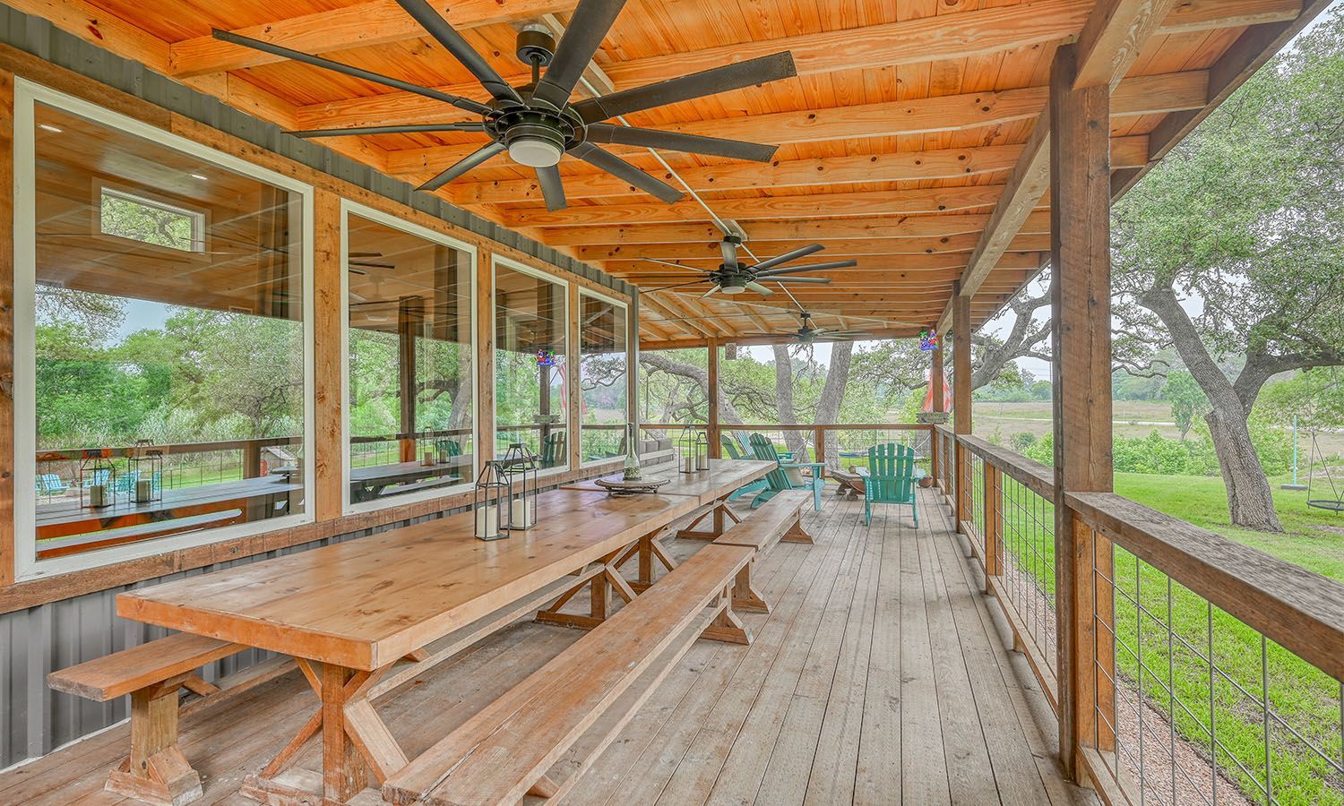 A wooden porch with a picnic table and benches and a ceiling fan.