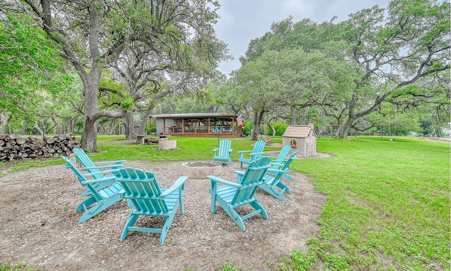 A group of blue chairs are sitting around a fire pit in a grassy field.