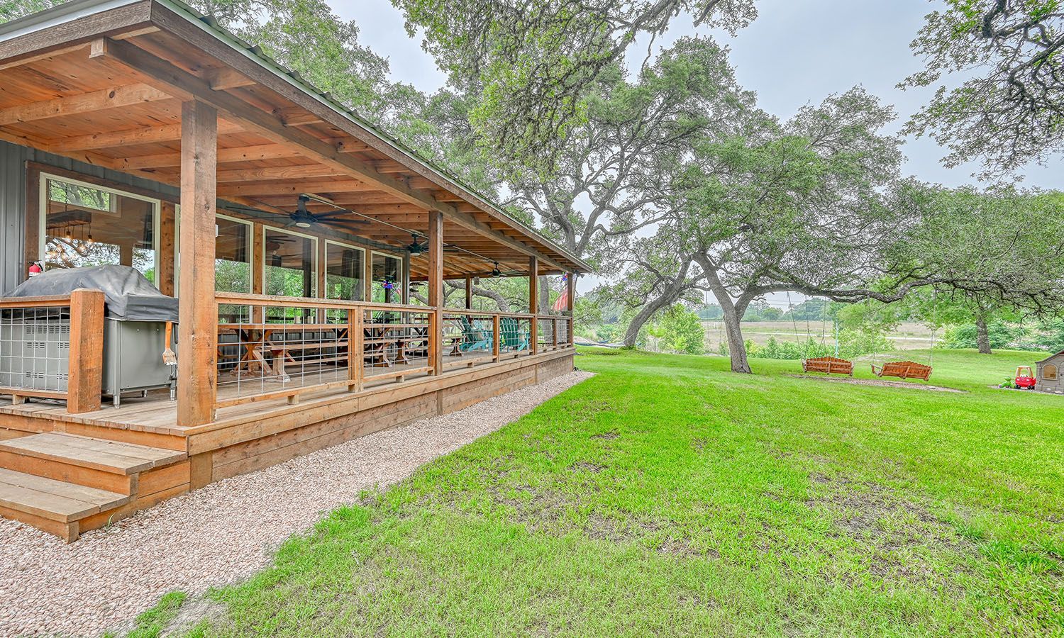 There is a large porch with a grill on it in the middle of a grassy field.