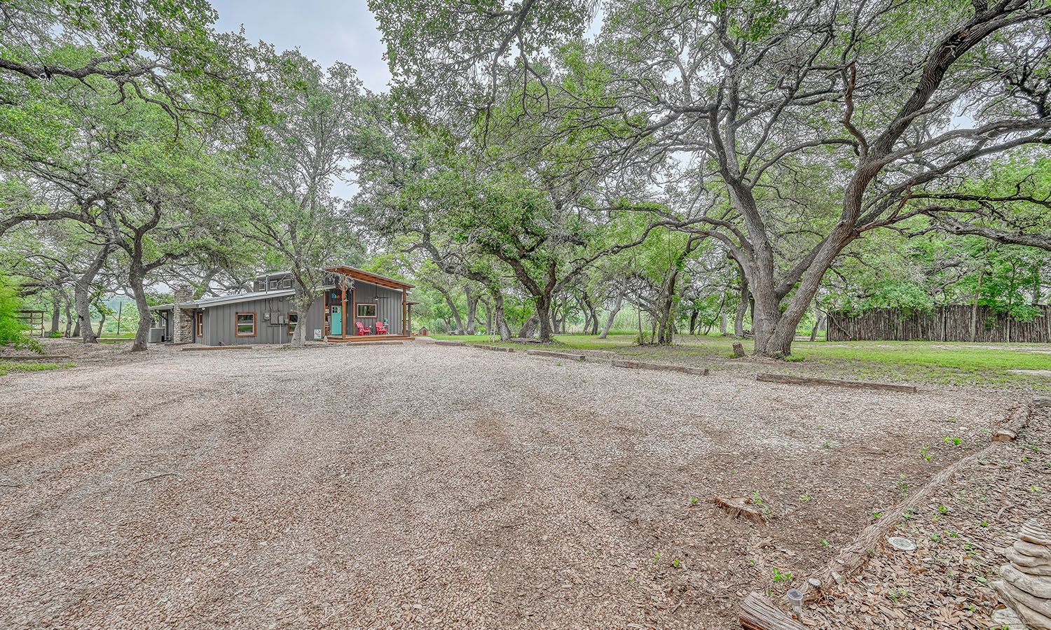 A house is surrounded by trees and a gravel driveway.