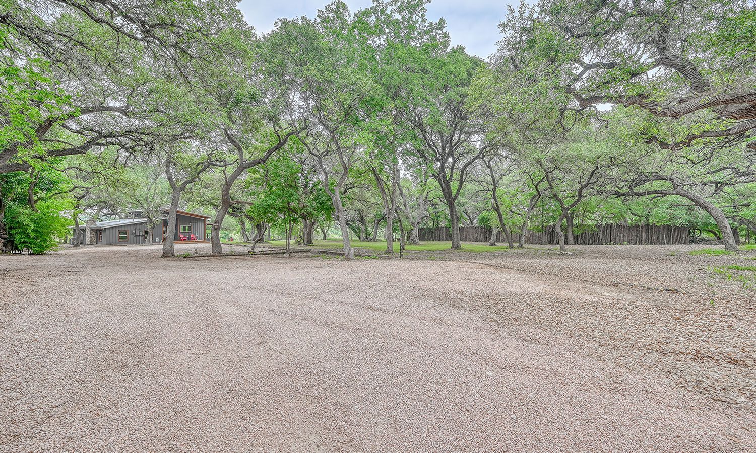 A dirt field with trees in the background and a house in the background.