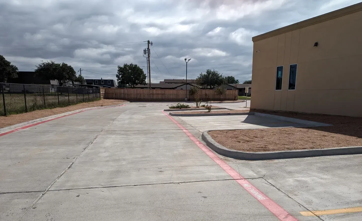 Empty concrete parking lot beside tan building under cloudy sky