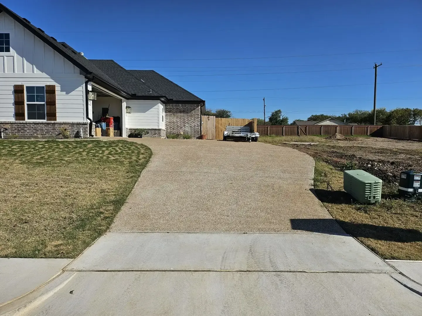 House with gravel driveway, small parked car, and fenced yard under a clear blue sky