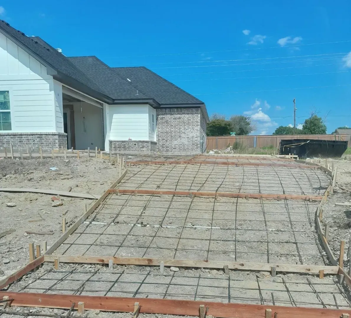 New house driveway under construction with rebar and concrete forms beside a stone exterior