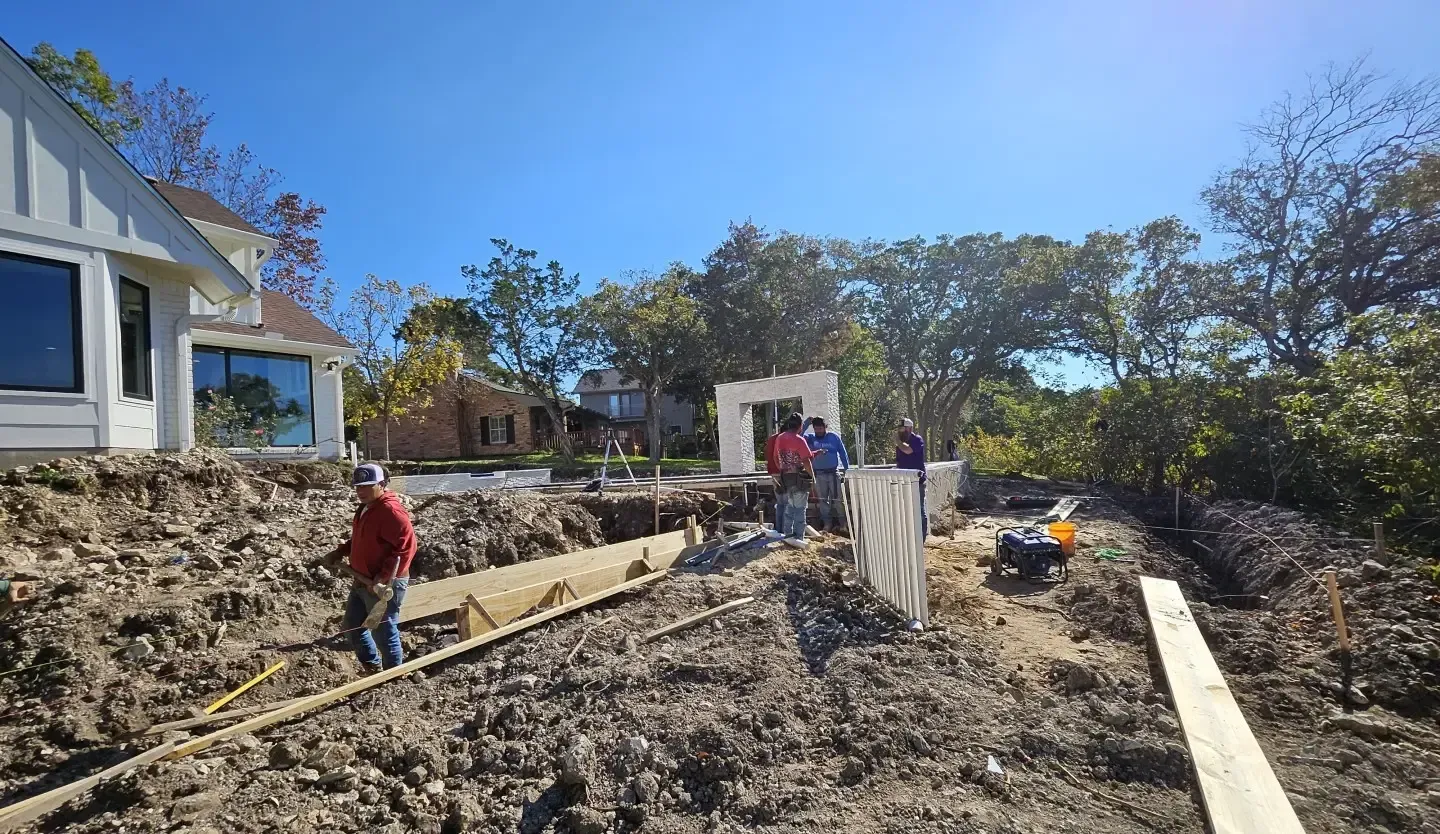 People working in a rocky yard beside a house under a bright blue sky