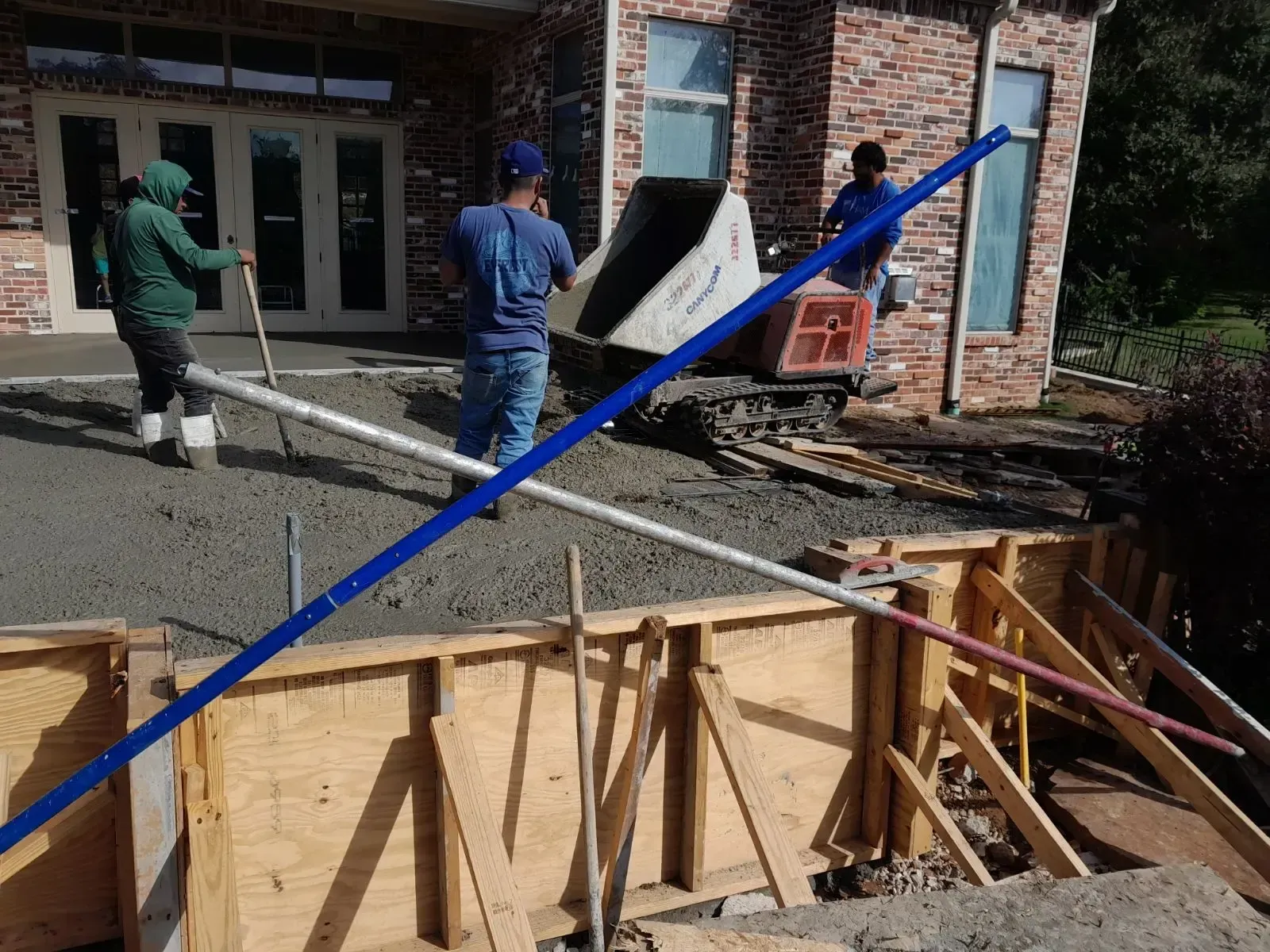 Workers pouring concrete into a wooden foundation frame at a construction site