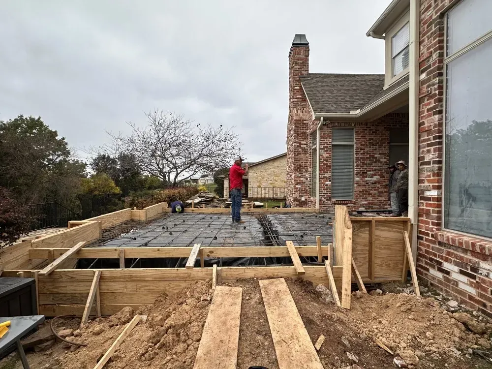 Construction site with a worker on a foundation beside a brick house and wooden framing