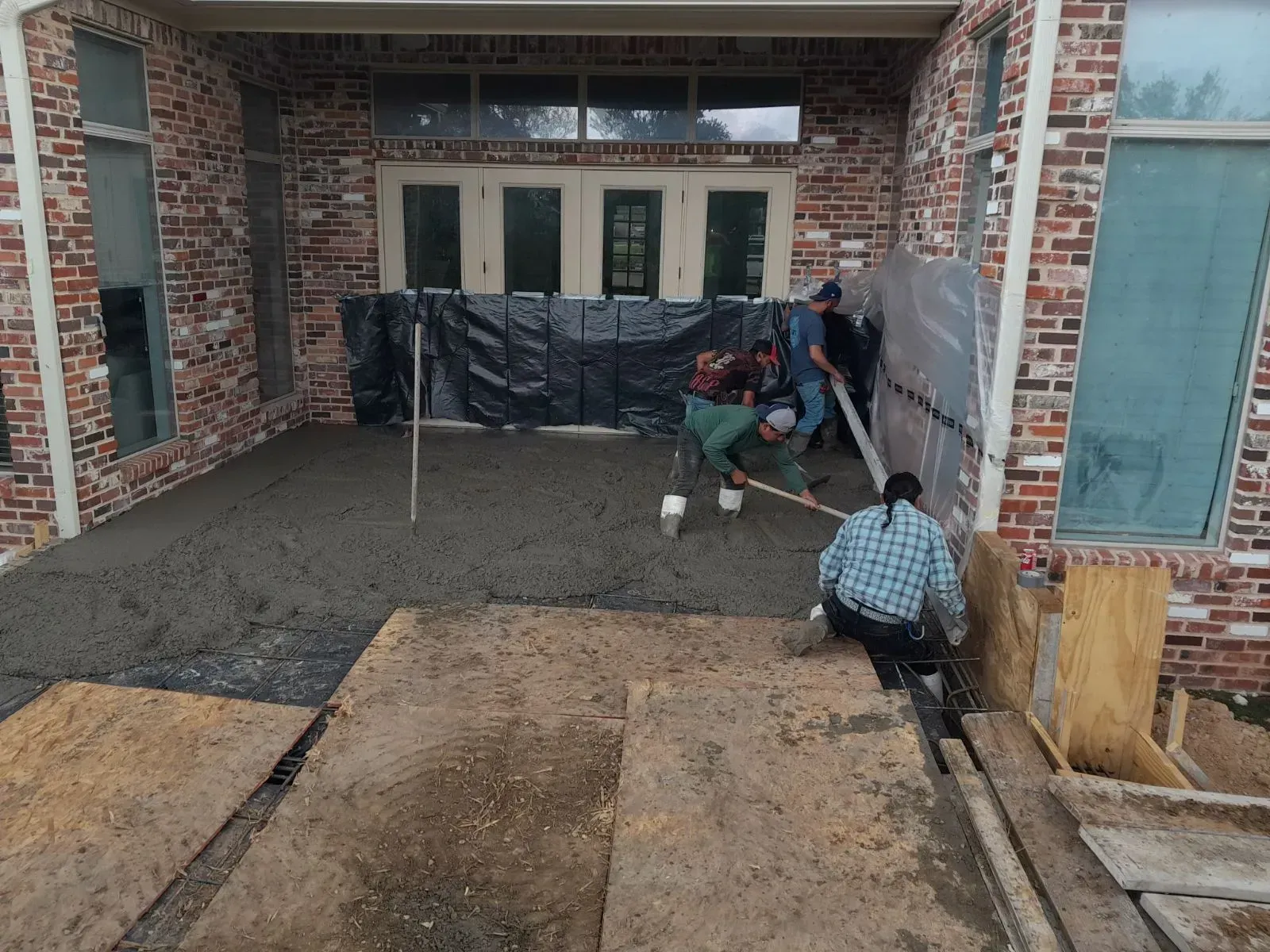 Workers pouring concrete in a brick courtyard beside a building under construction
