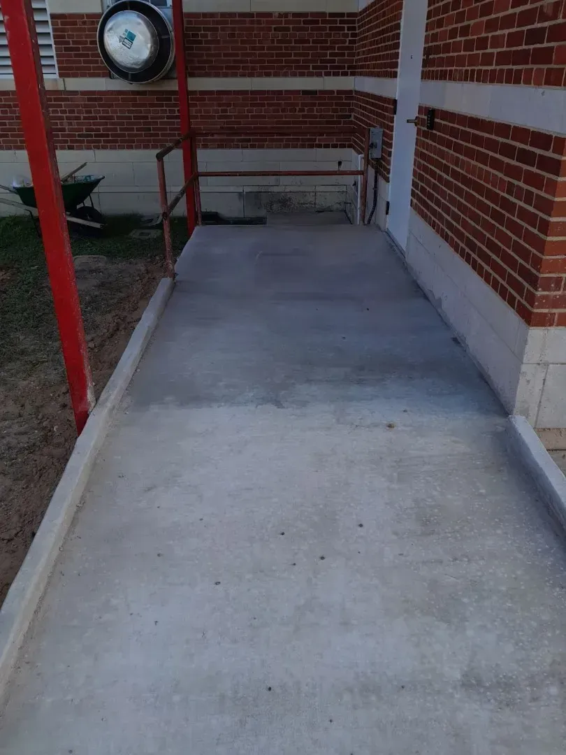 Covered concrete ramp beside brick building, with red railings and a round wall clock nearby