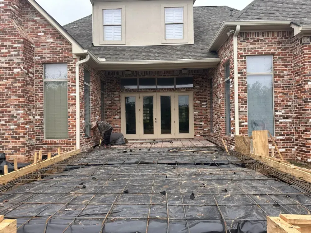 Front view of a brick house under construction with exposed foundation and wrapped porch area