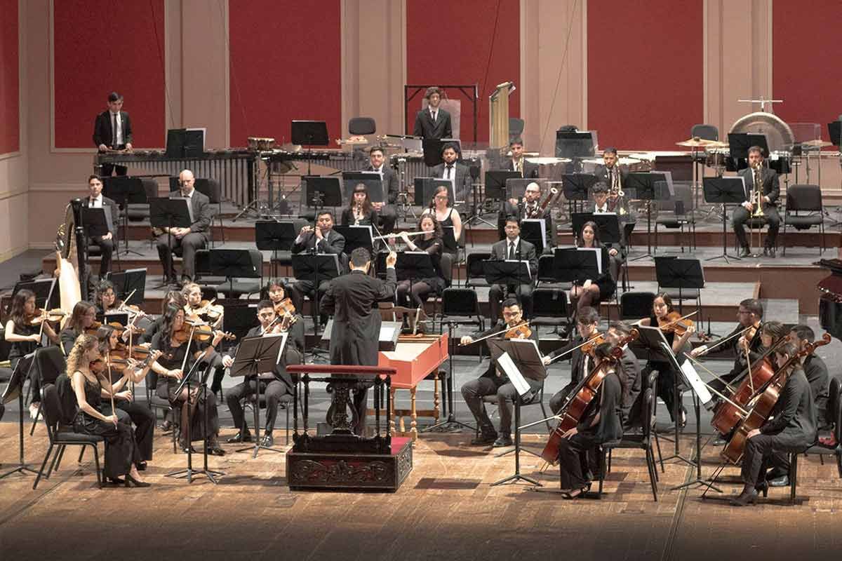 Una orquesta actuando en un escenario, con el director frente a los músicos.