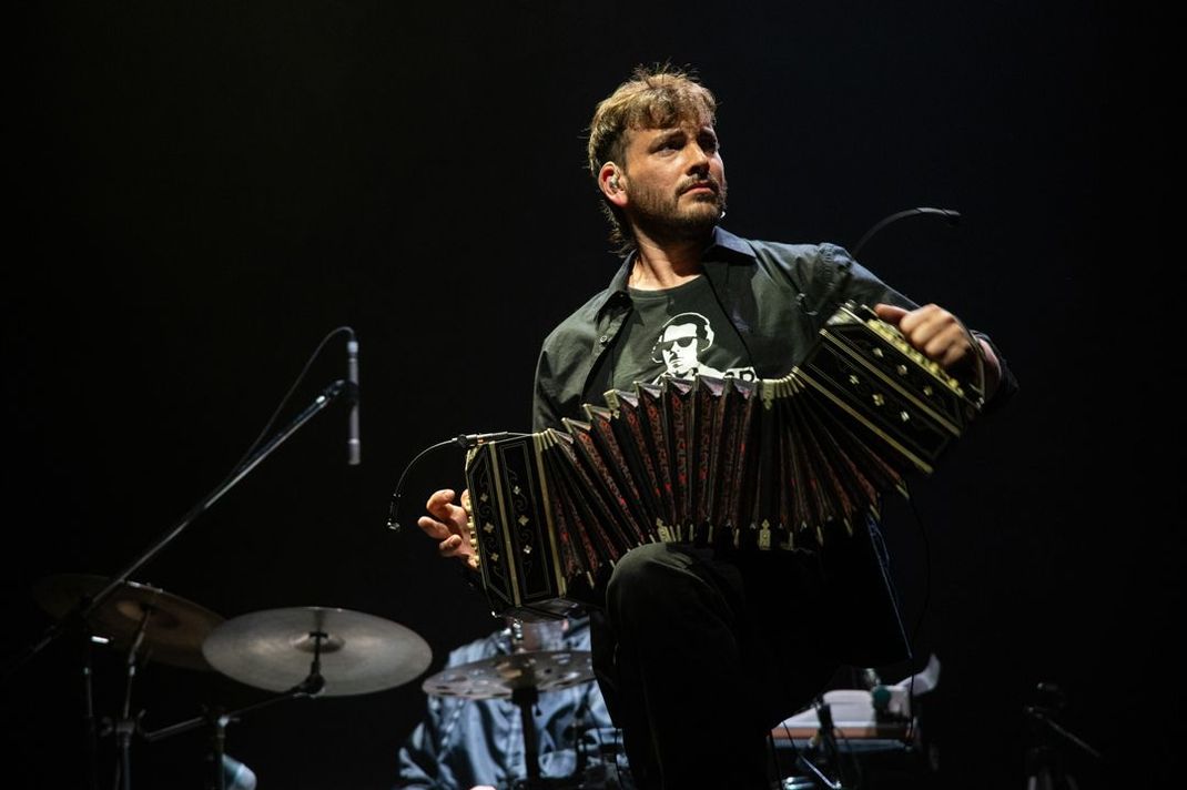 Hombre tocando el bandoneón en el escenario, actuando. Ambiente oscuro, ropa negra.
