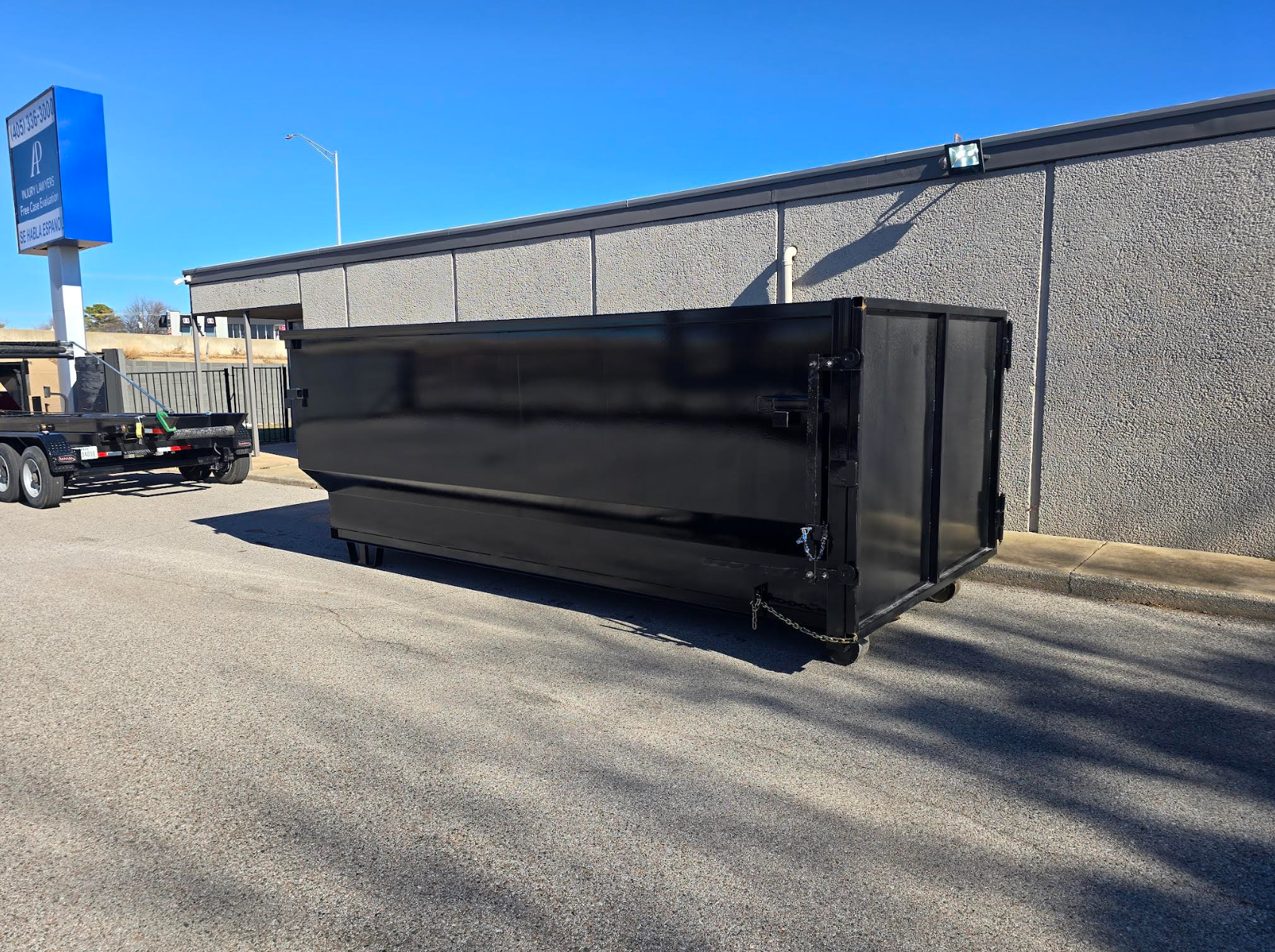 Blue dumpster in a parking lot, blocked by a caution sign, under a clear sky.