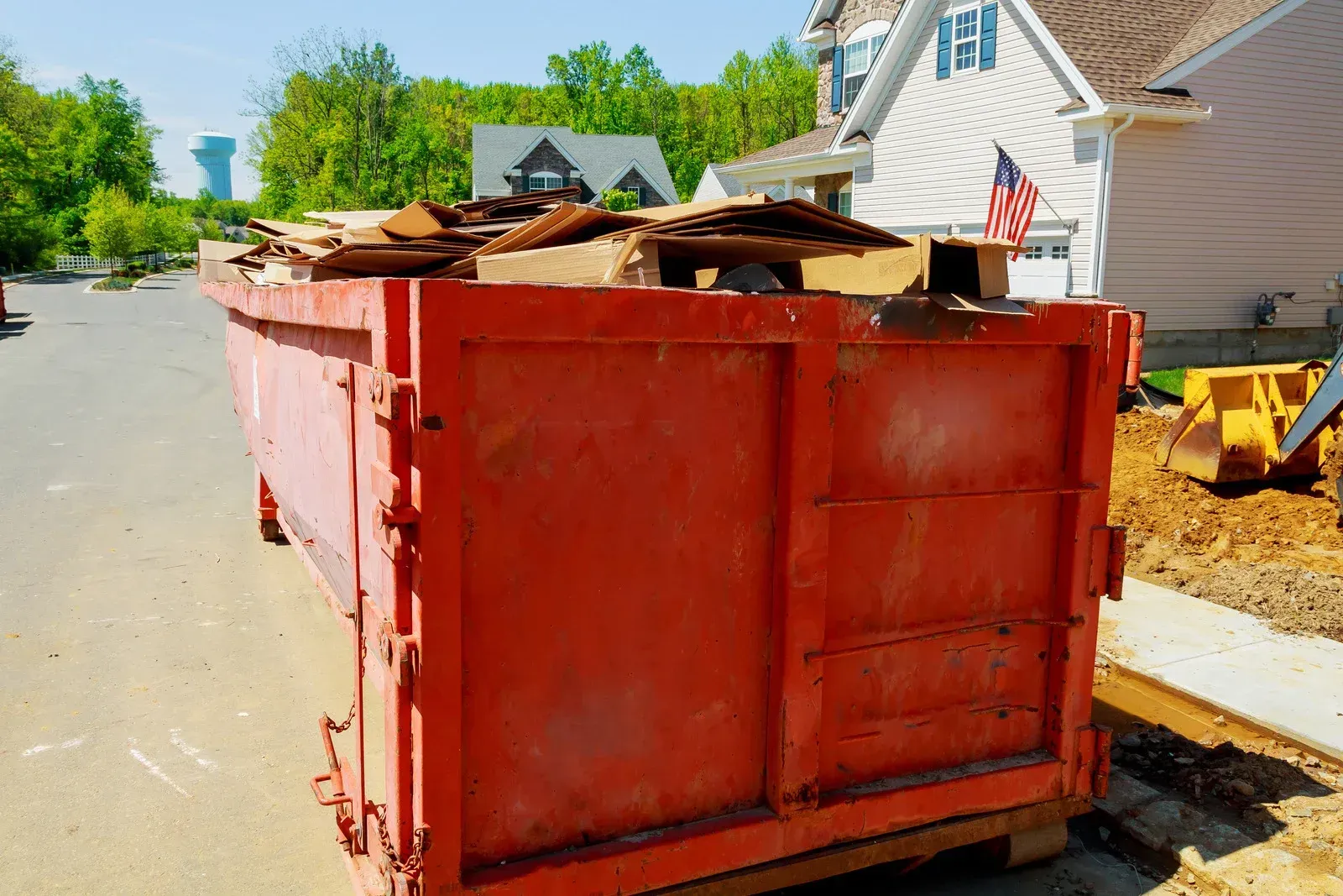 Red dumpster overflowing with debris on a street in a residential neighborhood.