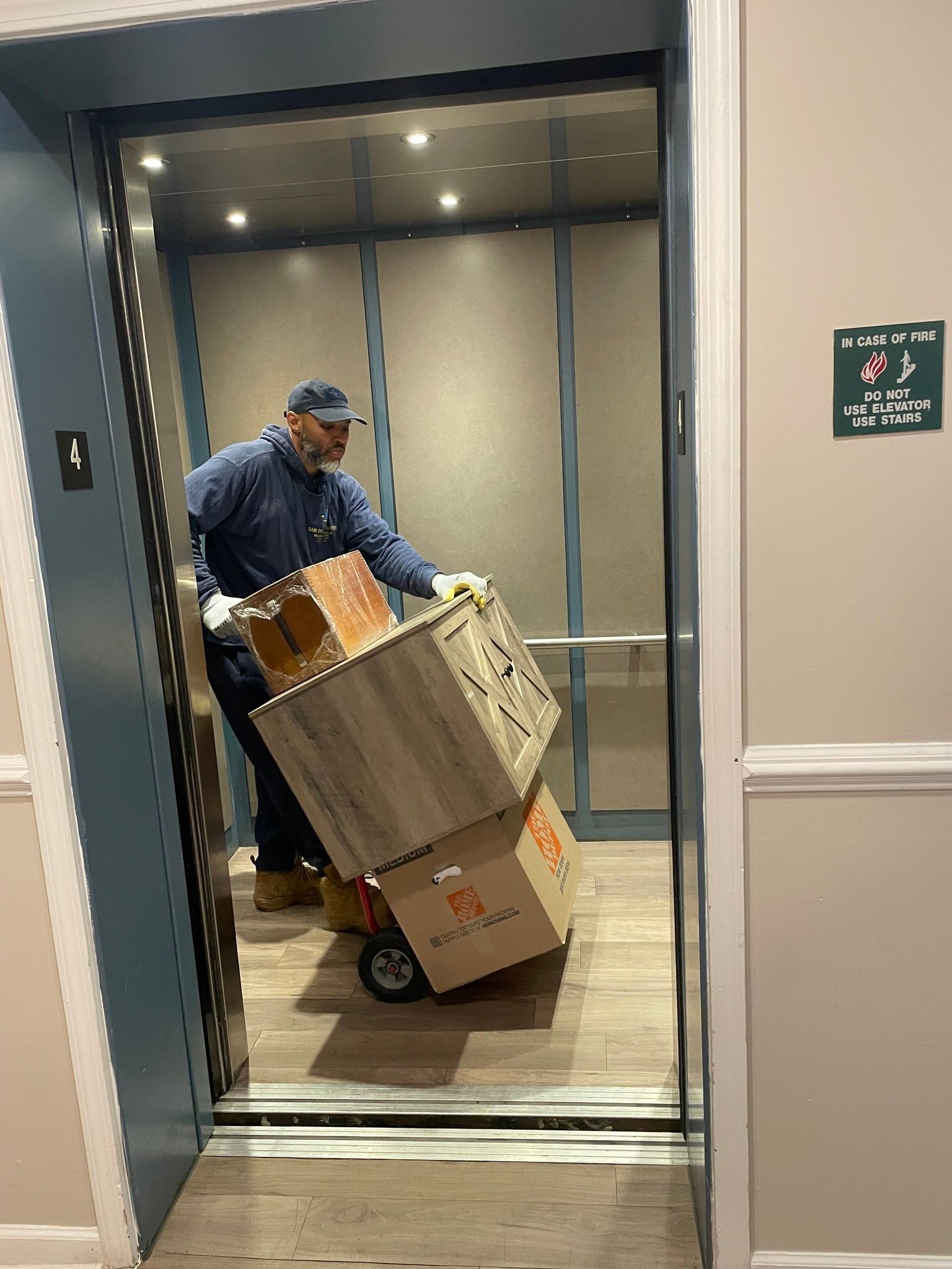 Man in blue uniform loads boxes onto a dolly in an elevator.