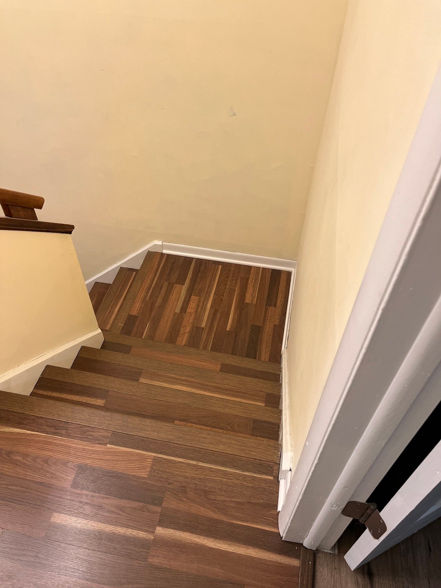 Staircase with wood-like flooring and beige walls. A white-framed door is in the right corner.