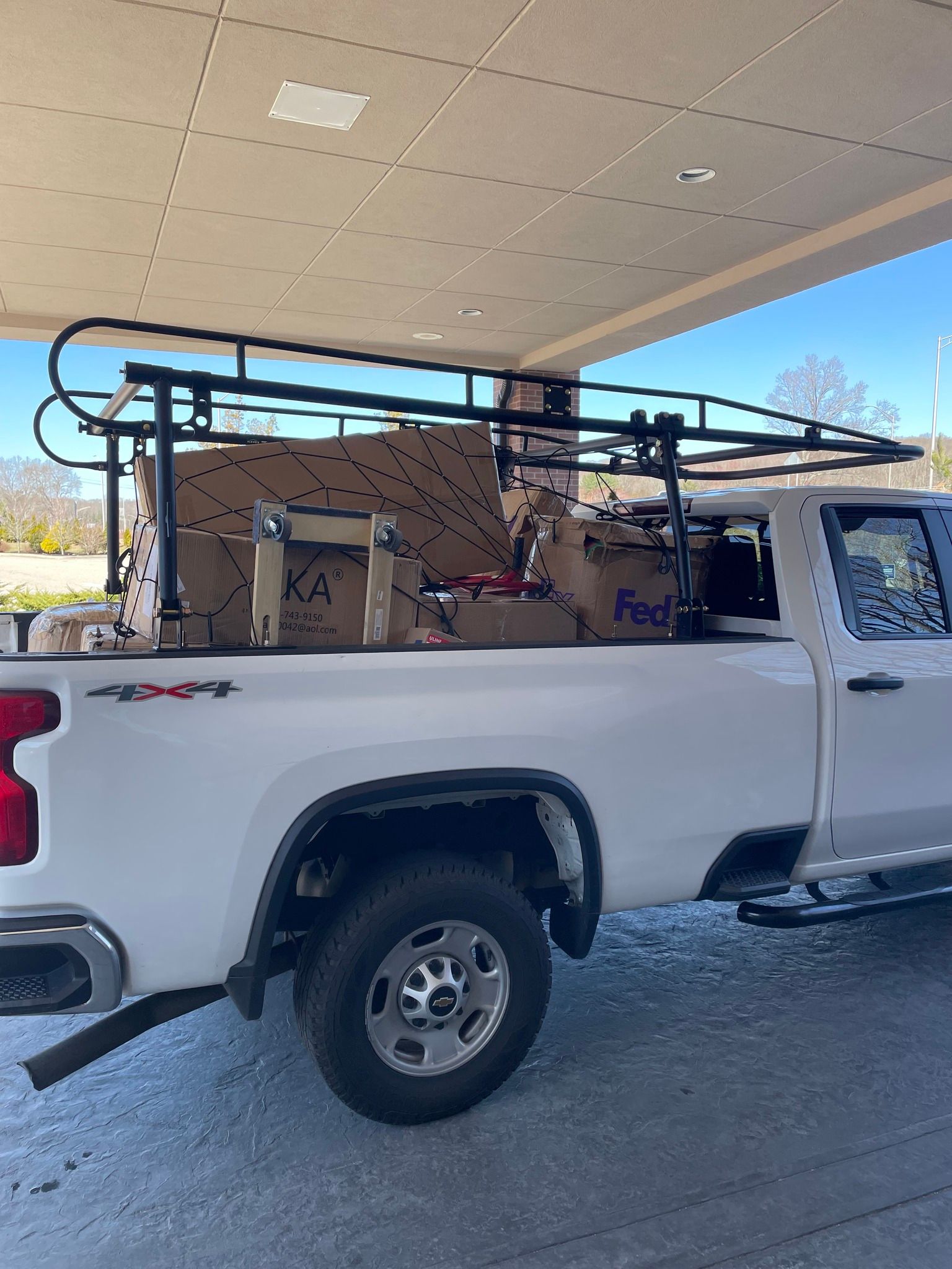 White pickup truck loaded with boxes under a black rack at a covered area.