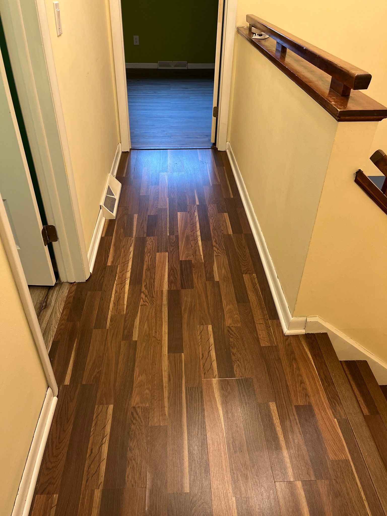 Hallway with dark wood floor, tan walls, and a staircase with a dark wooden handrail.