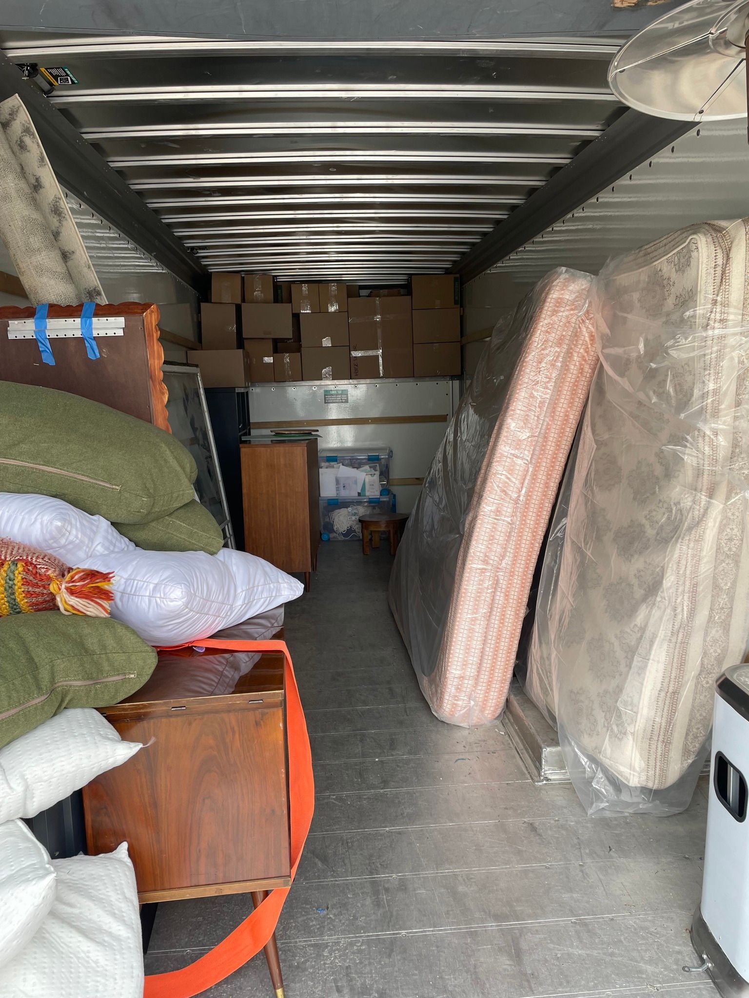 Inside a moving truck, filled with boxes, mattresses, and furniture.