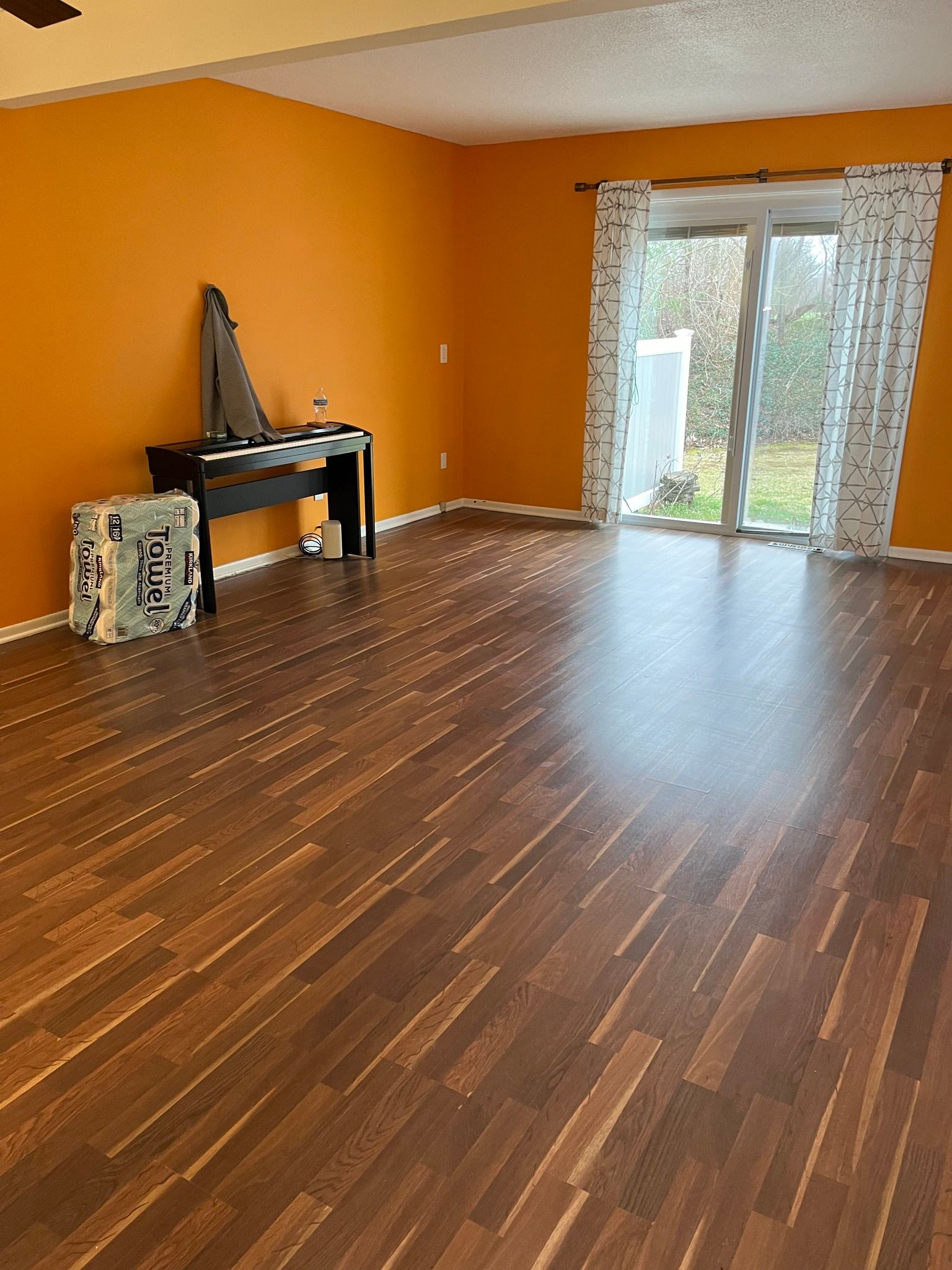 Room with orange wall, piano, sliding glass door, and wood-look flooring.