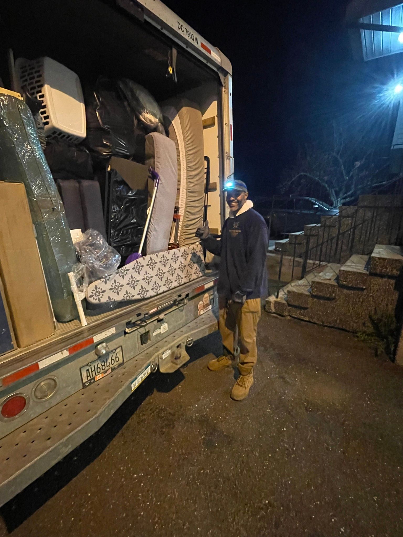 Man unloading truck at night. Boxes, furniture, and pavers are visible. Man has a headlamp.