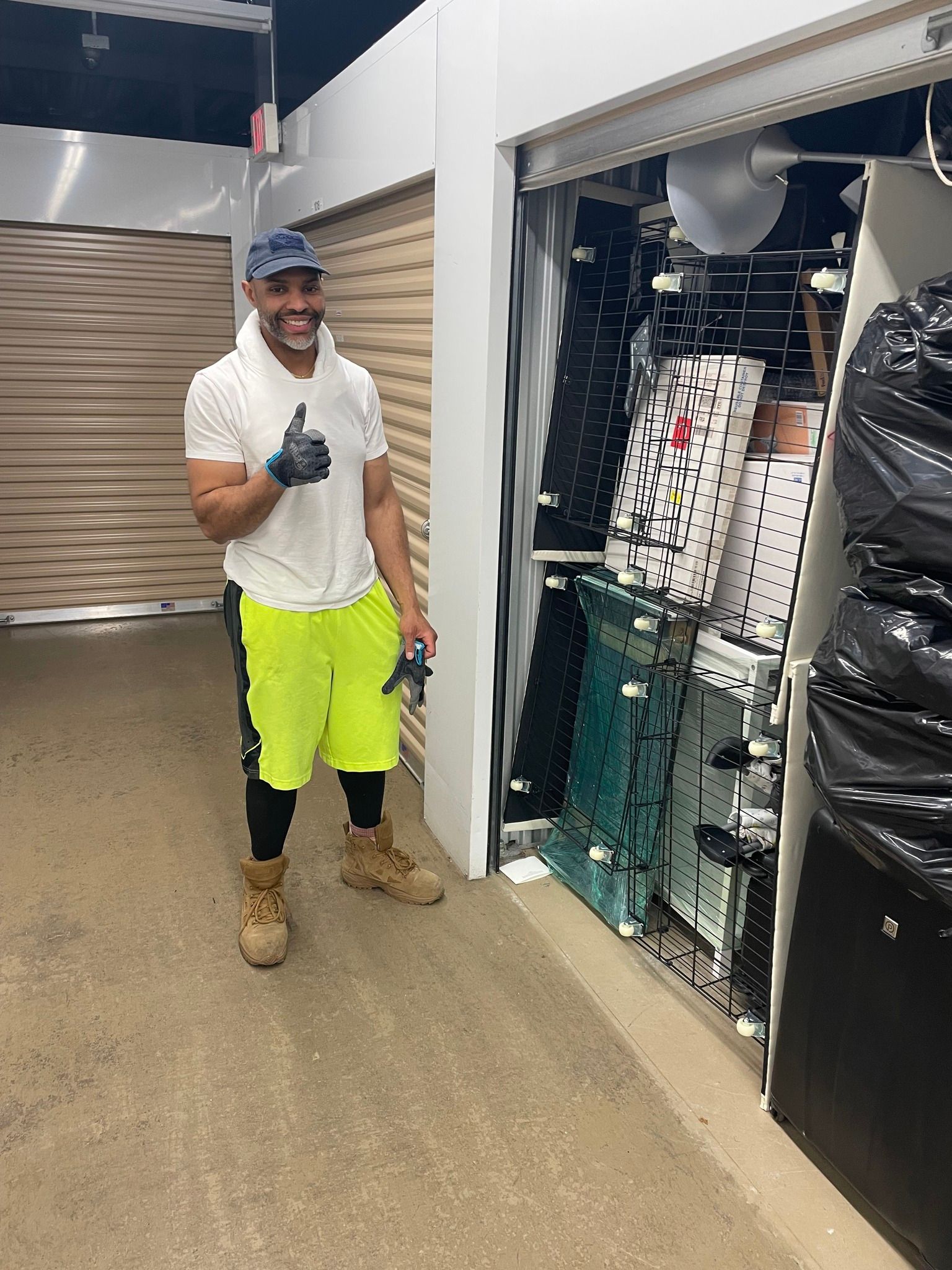 Man in neon shorts gives thumbs-up in front of storage unit filled with clothing.