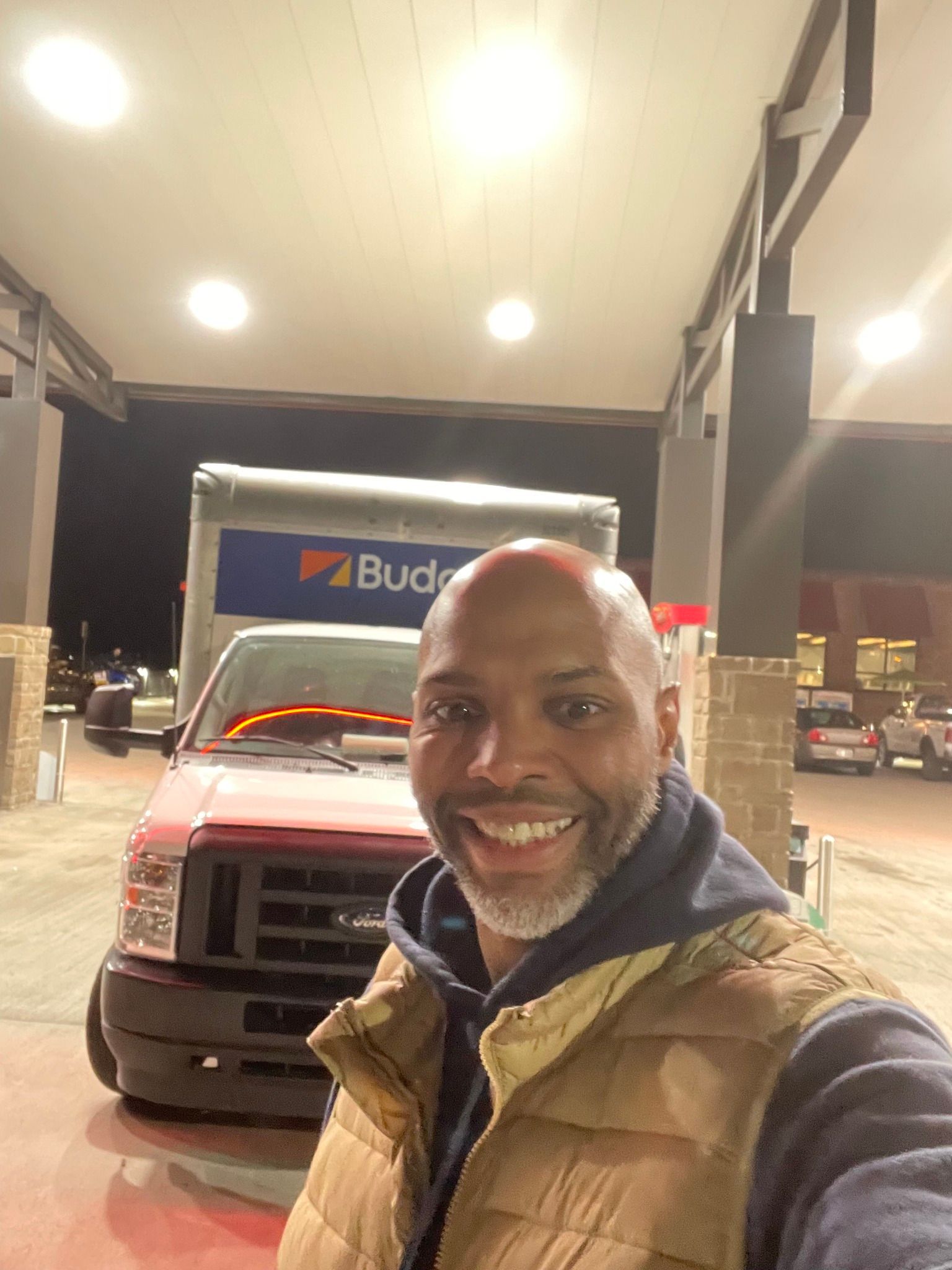 Man smiling in front of a Budget moving truck at a gas station.