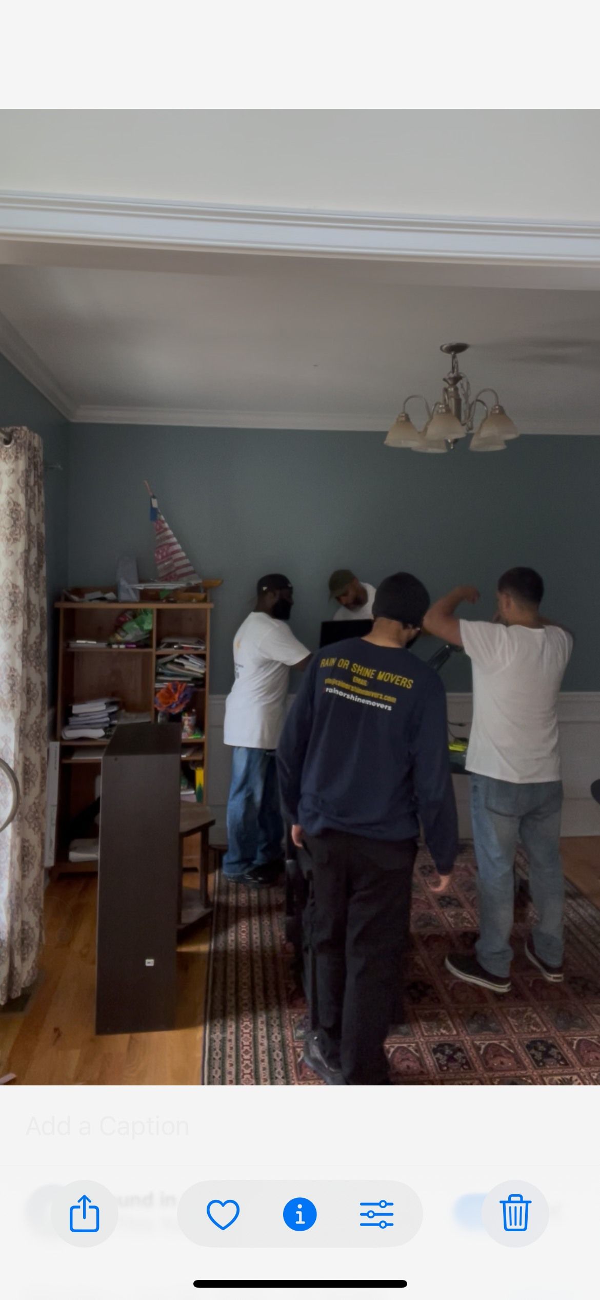 People in a room, one wearing a blue sweatshirt, next to a tall dark piece of furniture.