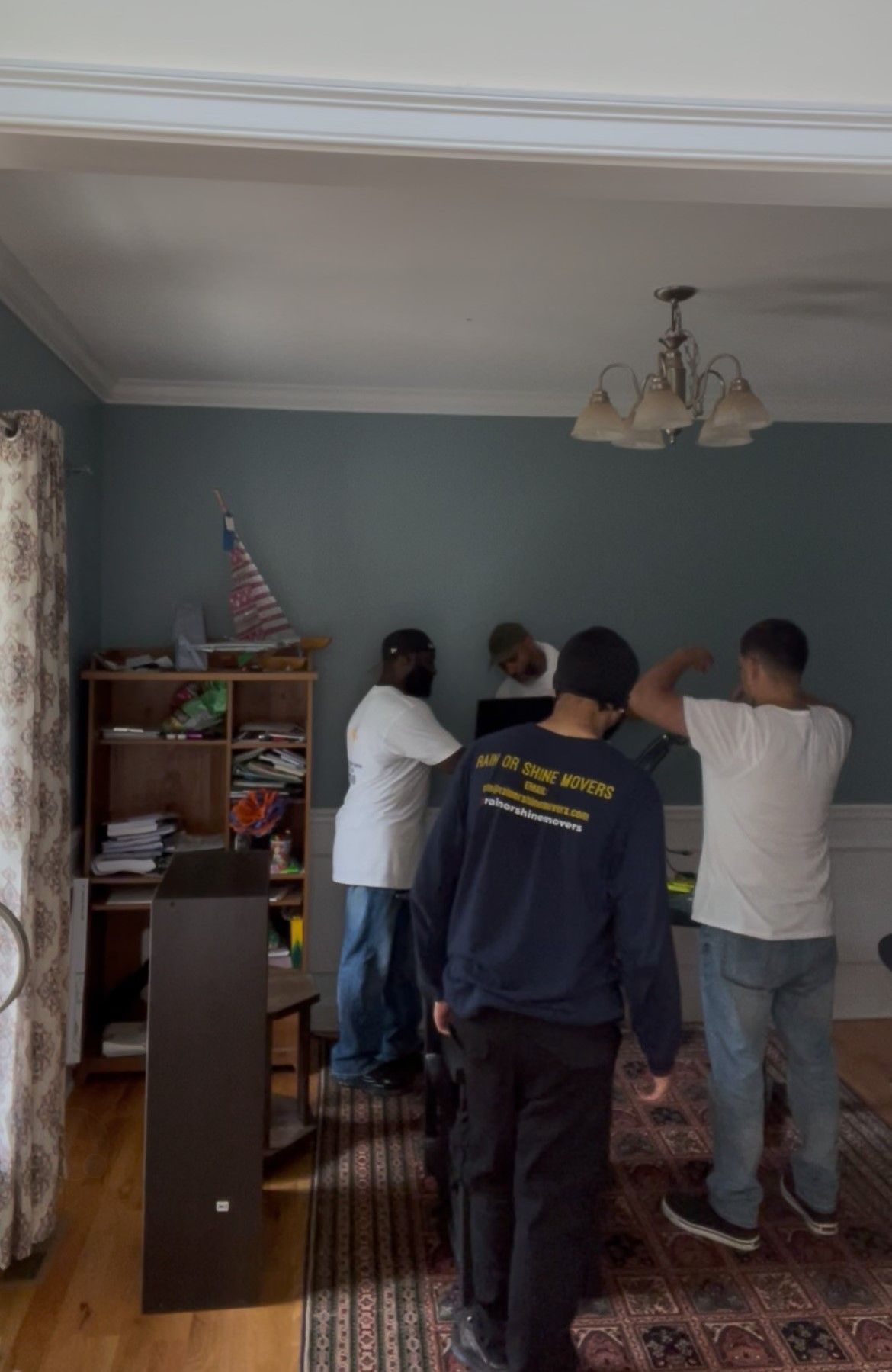 Movers inside a room with teal walls, removing a television. A bookshelf and rug are visible.