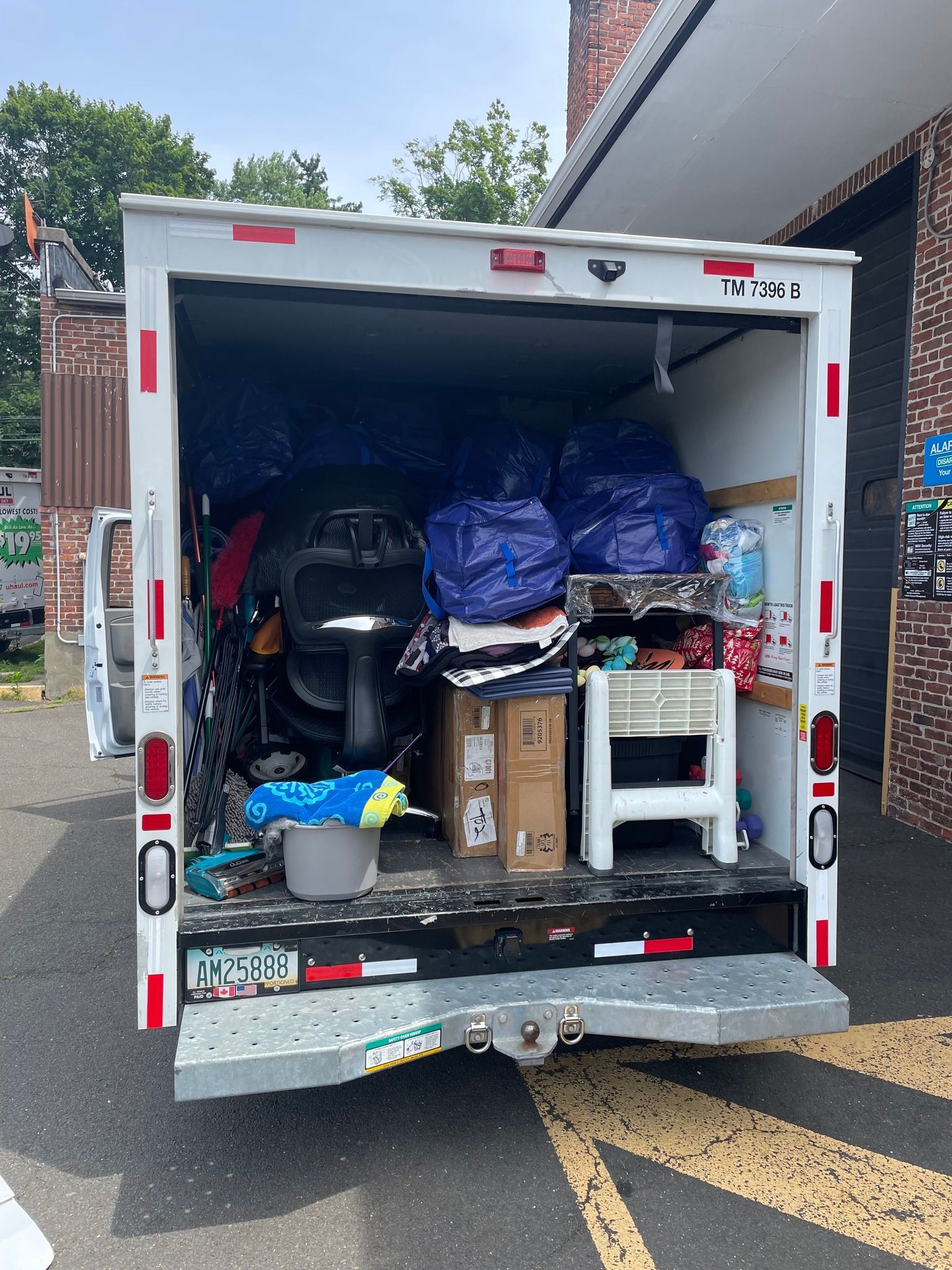 Open back of a white moving truck filled with boxes, bags, and various household items, parked outside.