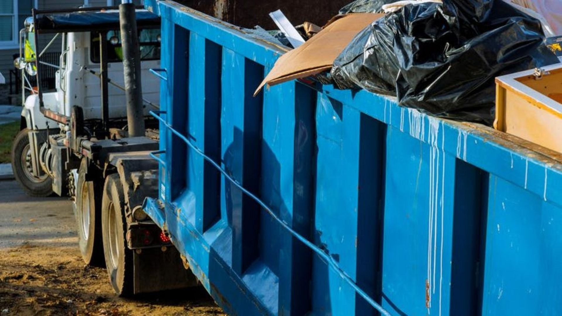 Blue dumpster filled with trash, loaded on a truck, outdoors.