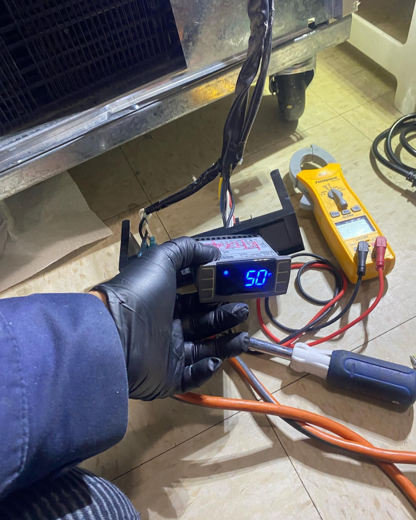 A person wearing black gloves is holding a digital thermometer in their hand.