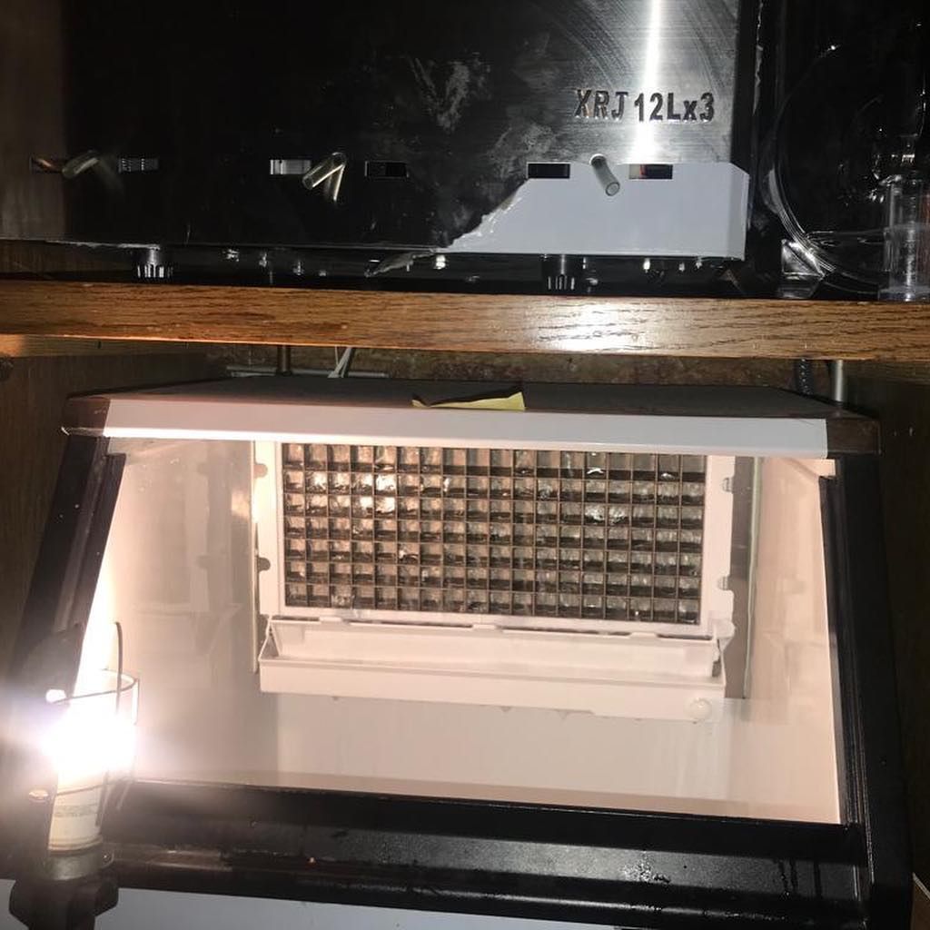 A stainless steel ice maker is sitting on top of a wooden shelf.