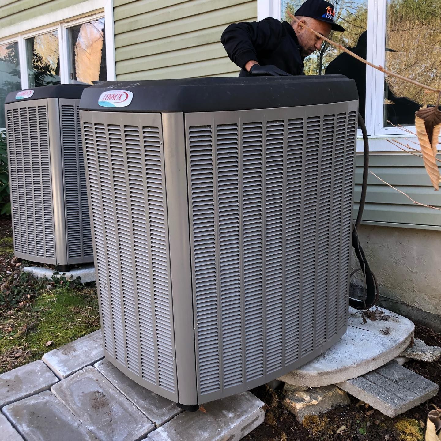 A man is working on an air conditioner outside of a house.