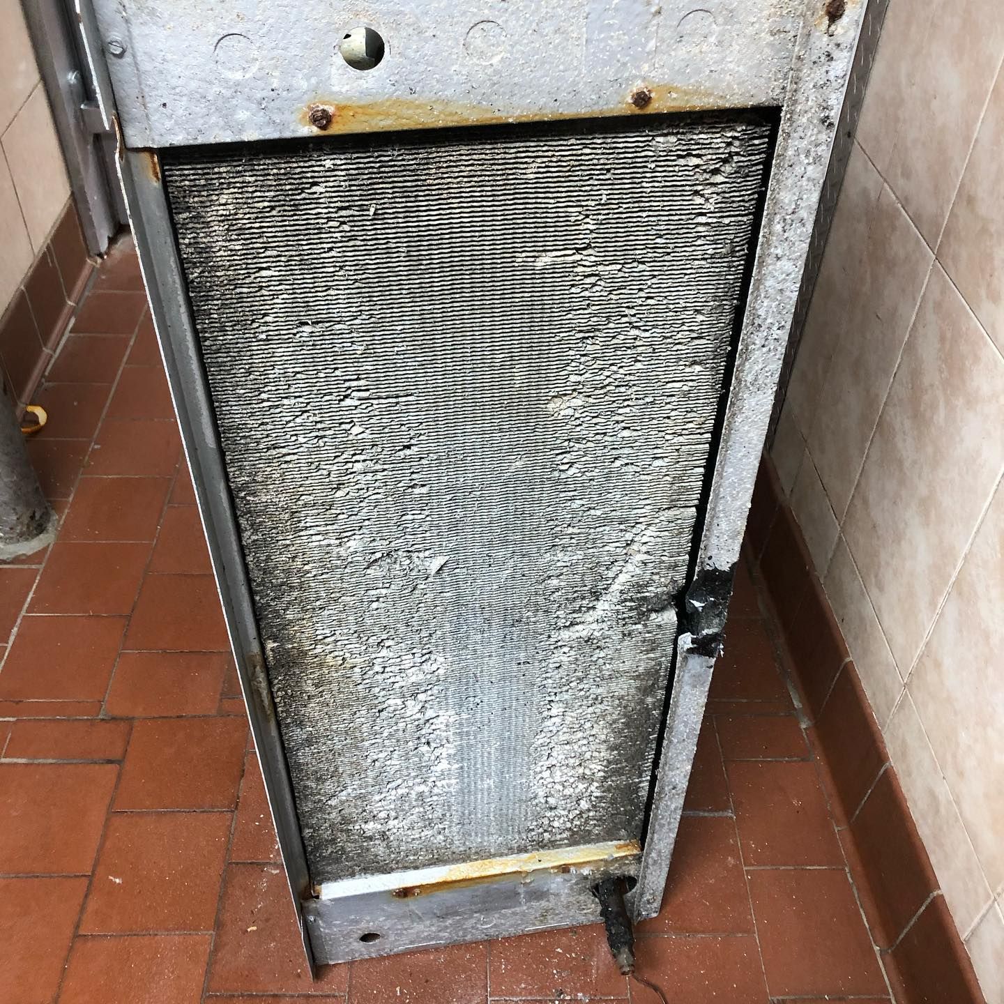 A dirty metal item is sitting on a tiled floor next to a wall.