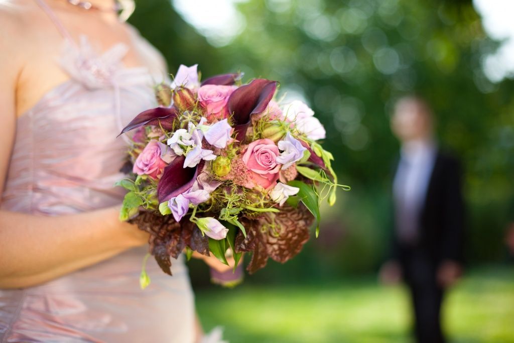 Eine Braut in einem rosa Kleid hält einen Blumenstrauß.