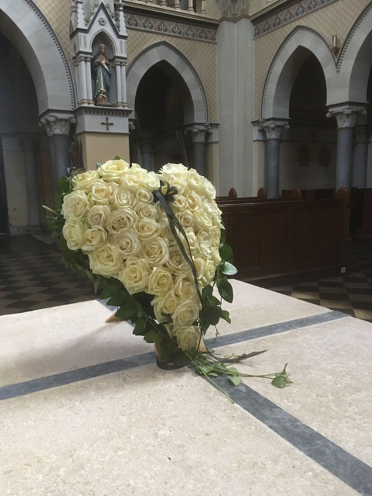 Auf einem Tisch in einer Kirche steht eine herzförmige Vase mit weißen Rosen.