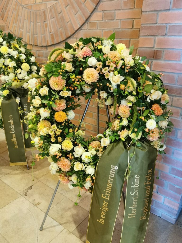 Ein großer Blumenkranz liegen auf einem Ständer vor einer Backsteinmauer.