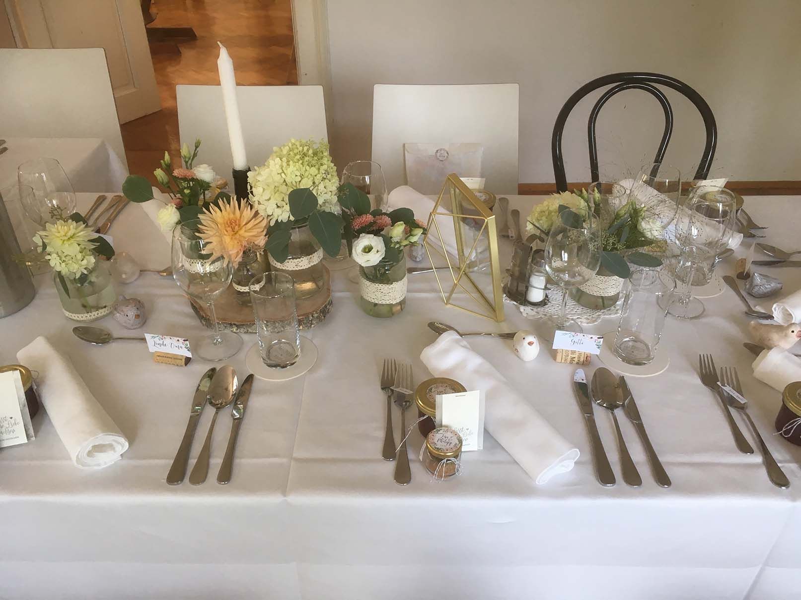 Ein für einen Hochzeitsempfang gedeckter Tisch mit Blumen und Kerzen darauf.