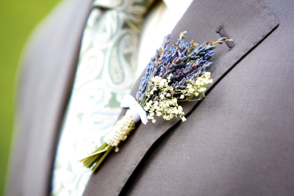 Ein Mann in Anzug und Krawatte trägt eine lavendelfarbene Ansteckblume an seiner Jacke.