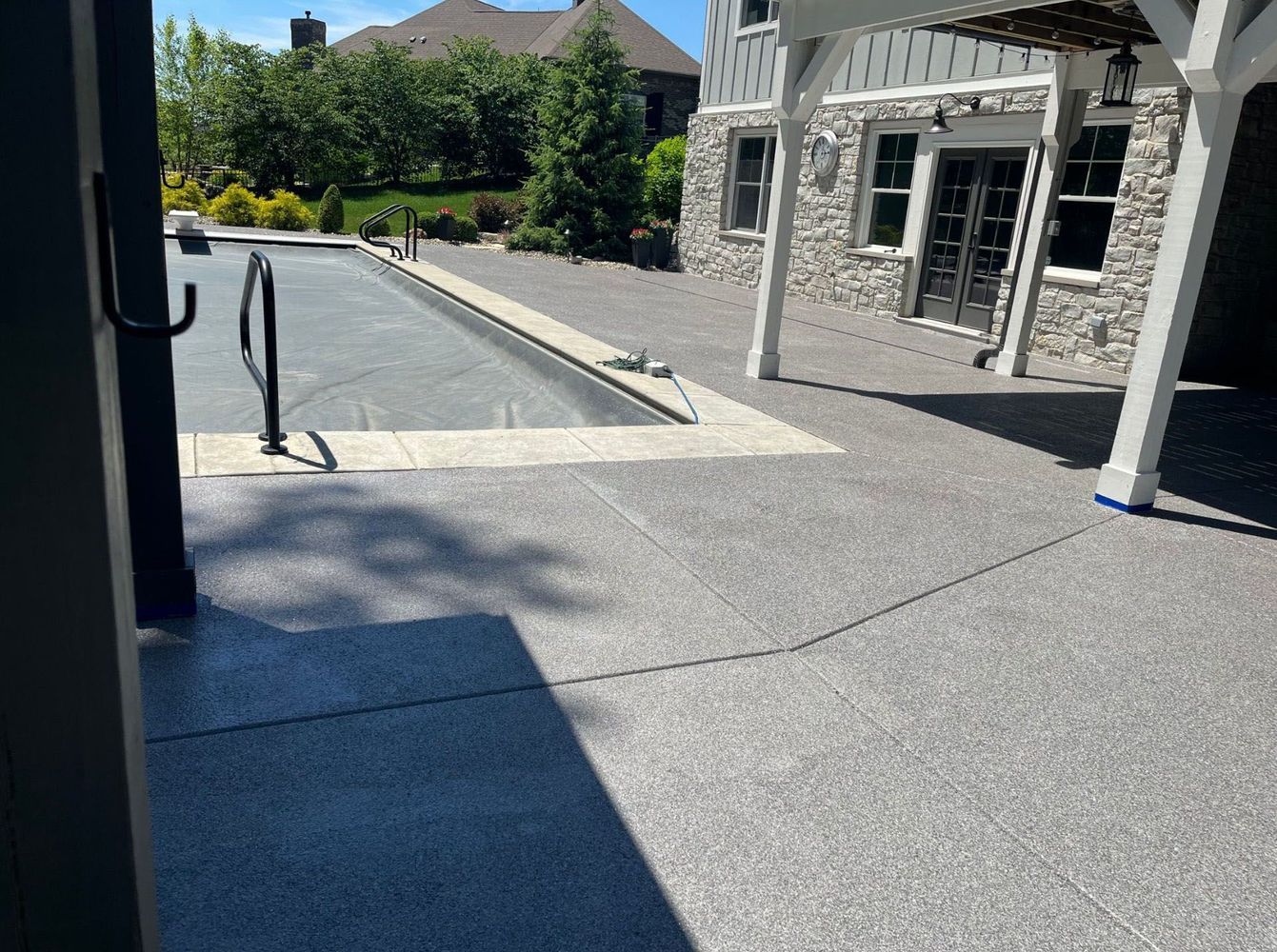 There is a large swimming pool surrounded by concrete in the backyard of a house.