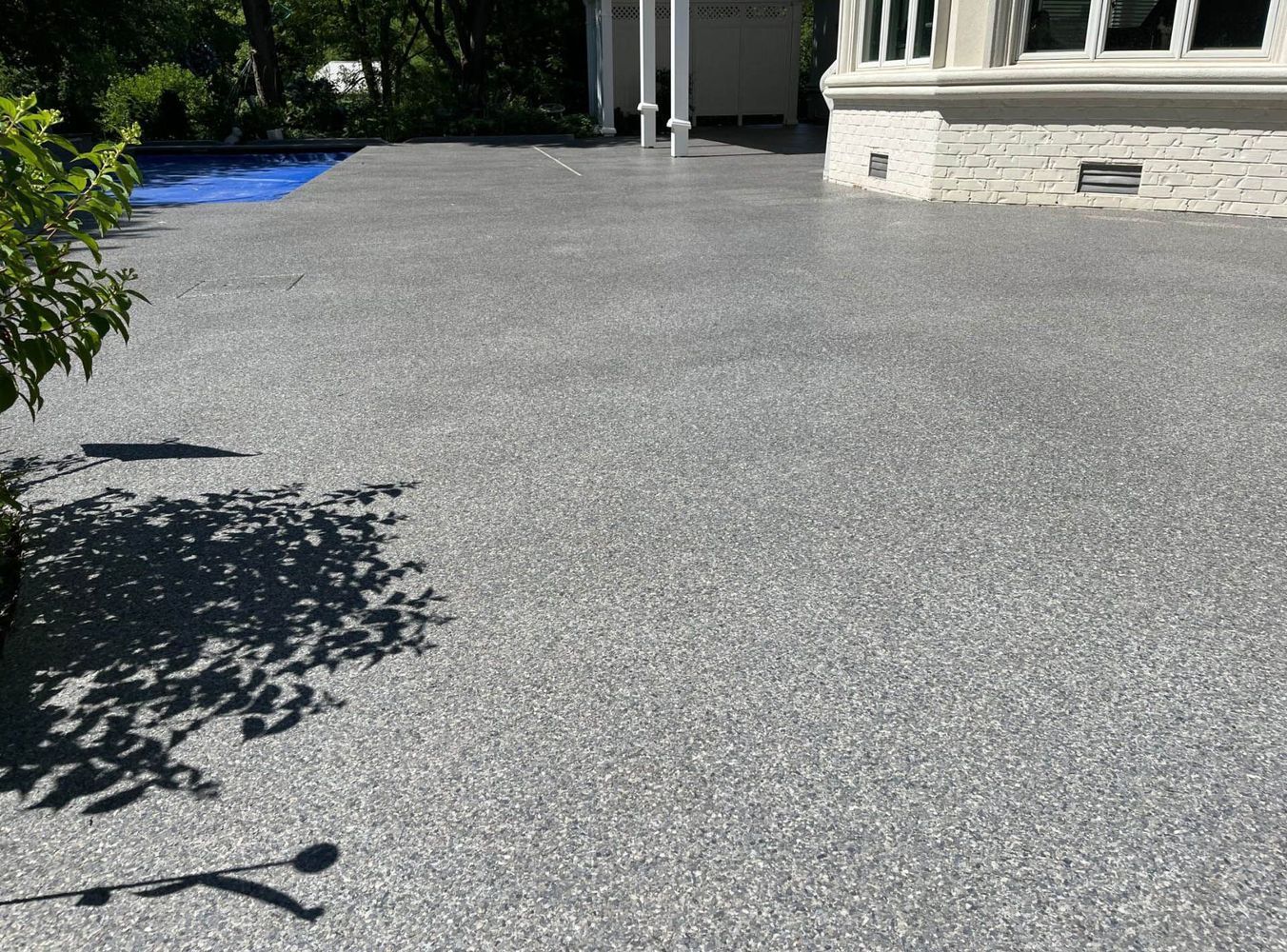 A concrete driveway in front of a house with a pool in the background.