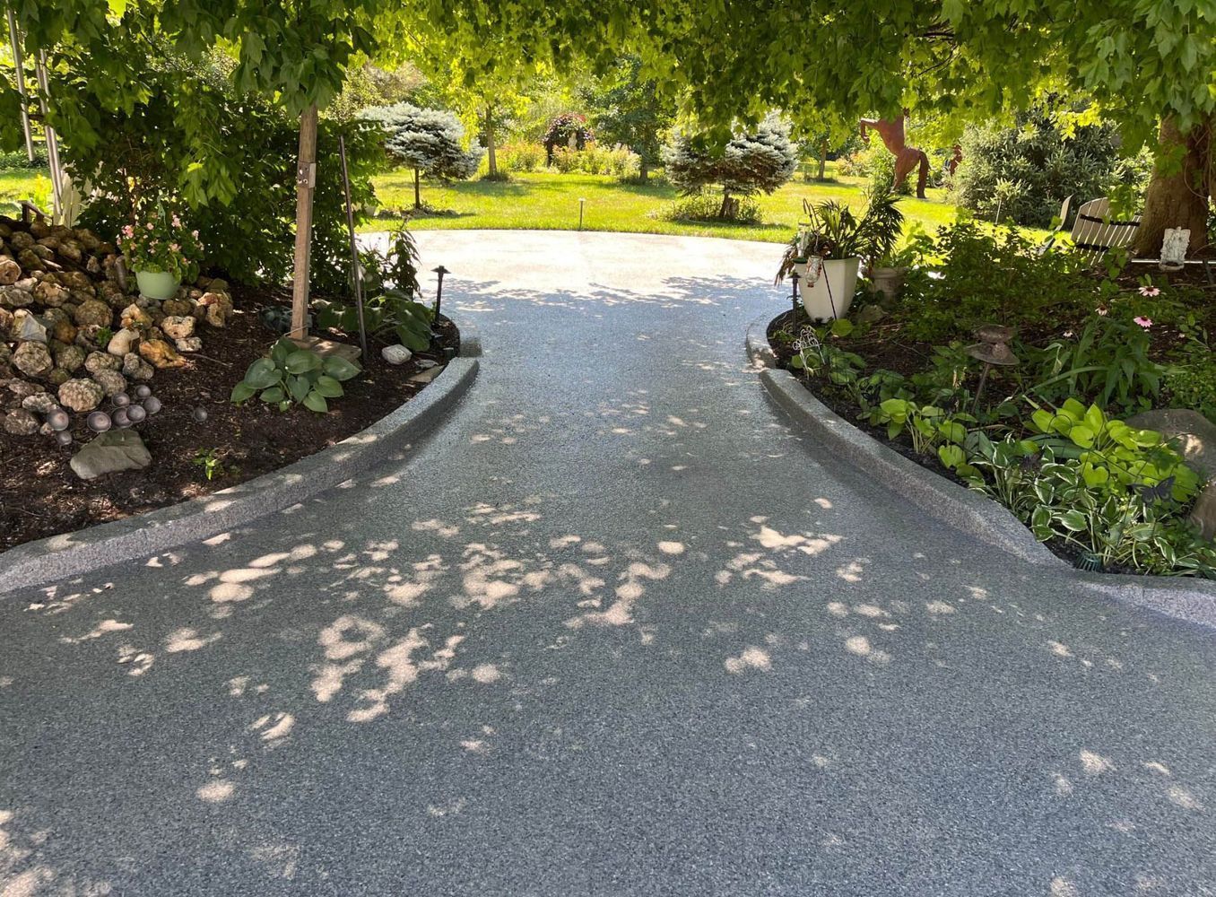 A concrete driveway leading to a garden with trees and bushes on both sides.