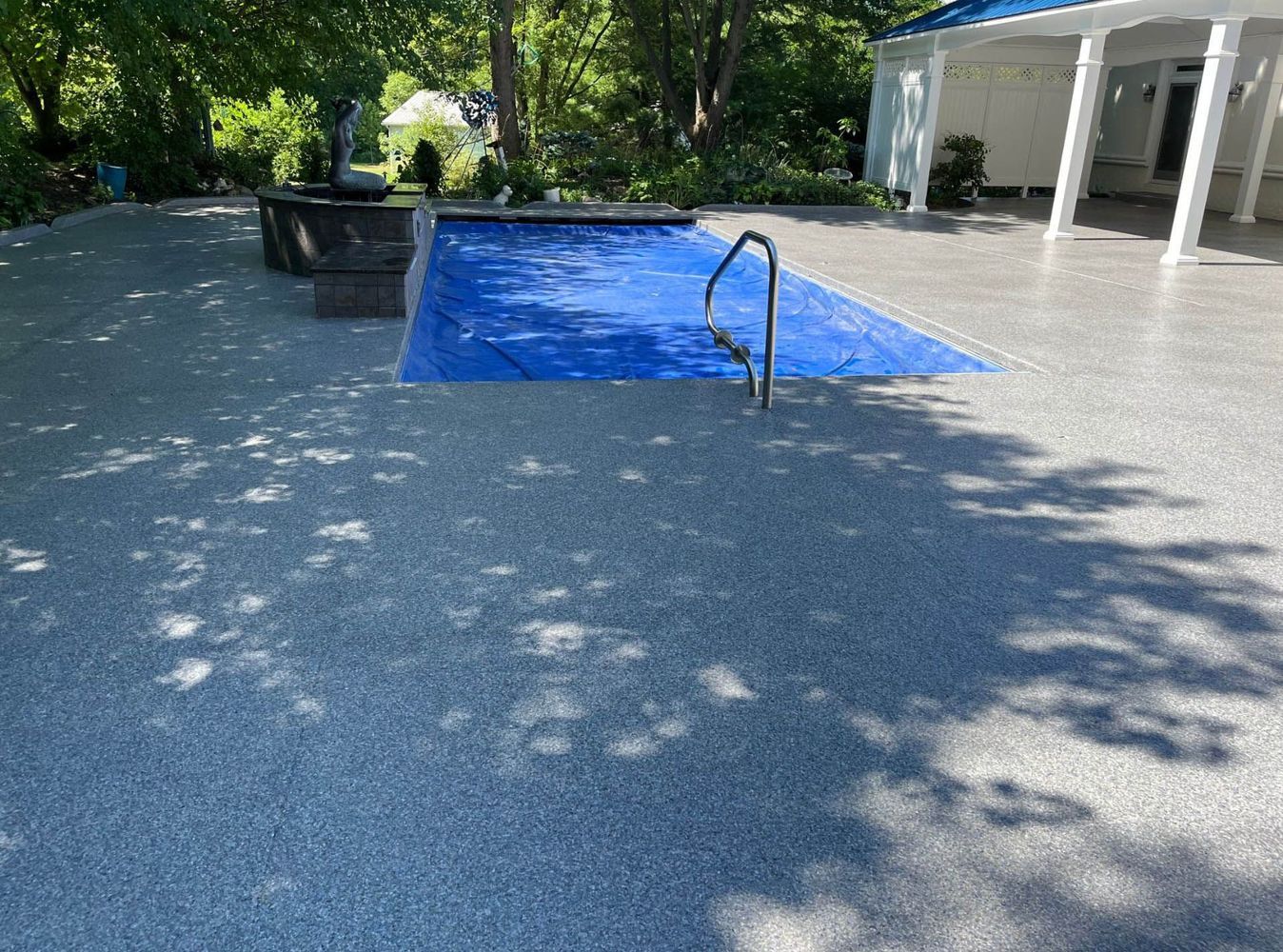 There is a large swimming pool surrounded by concrete in the backyard of a house.